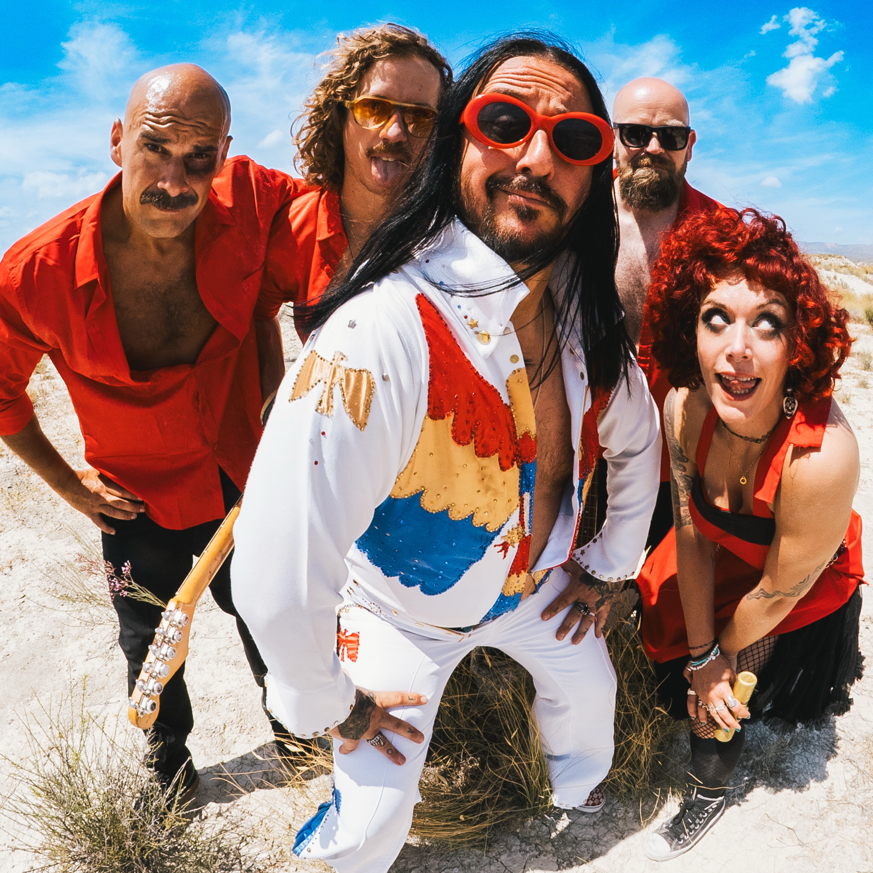Elvana band members in colorful outfits pose in a desert landscape.