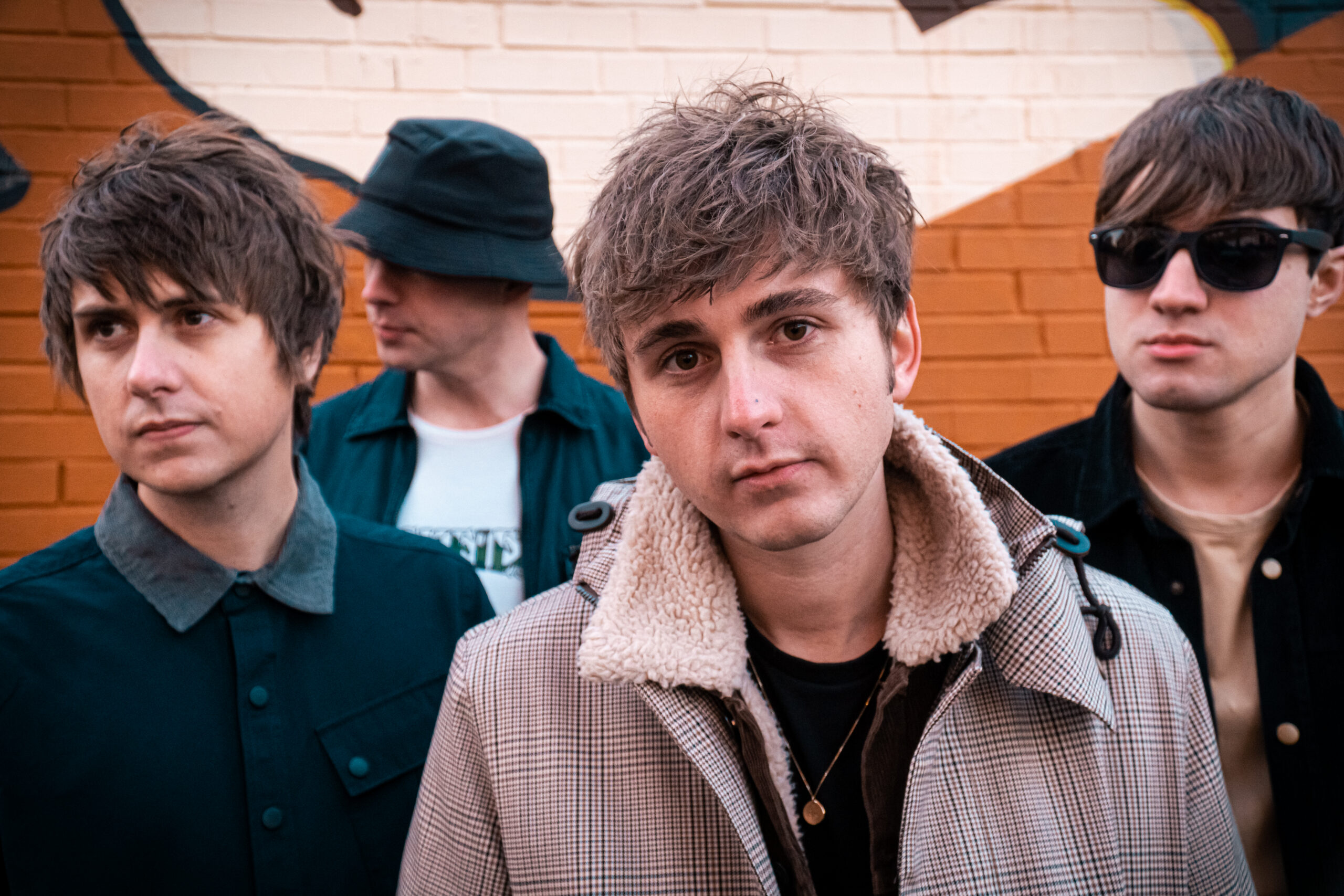 The Sherlocks band members pose for a portrait in front of a brick wall.